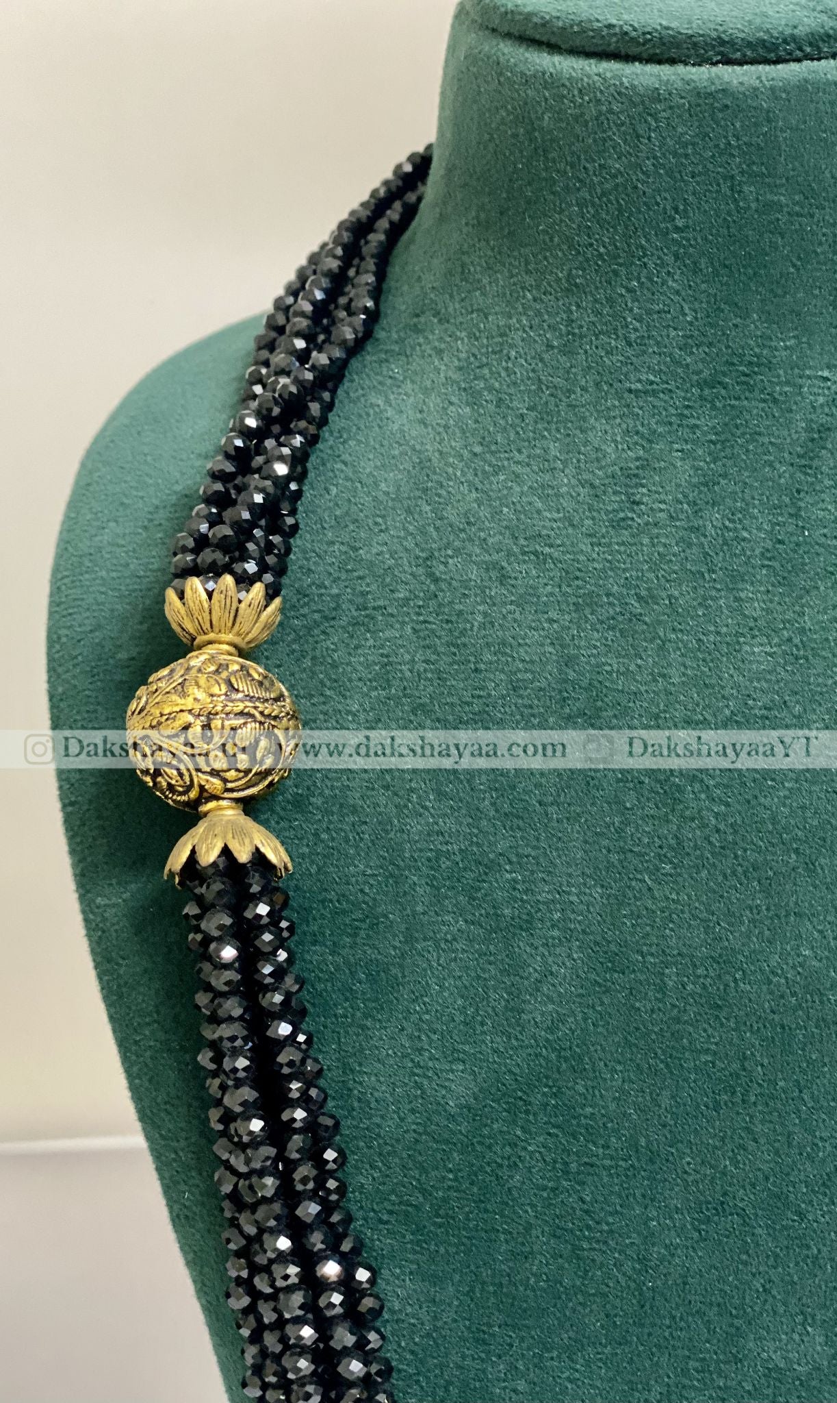 Black beaded necklace with a gold pendant on a green mannequin