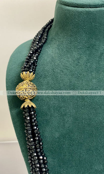 Black beaded necklace with a gold pendant on a green mannequin