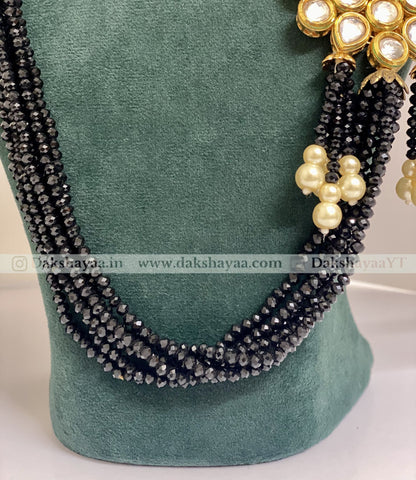 Black beaded necklace with gold and pearl accents on a green velvet stand.