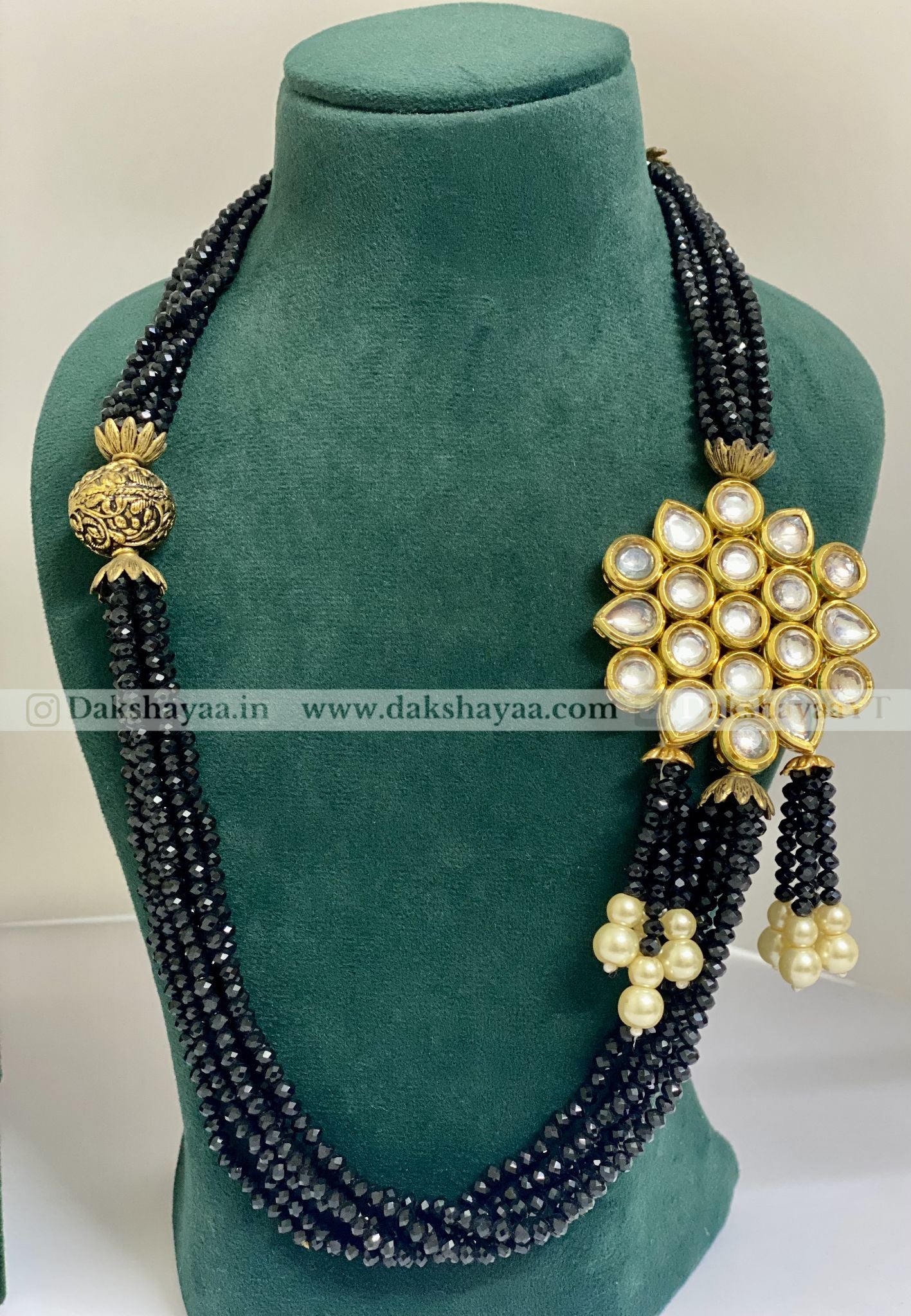Black beaded necklace with gold and pearl decorations on a green mannequin.