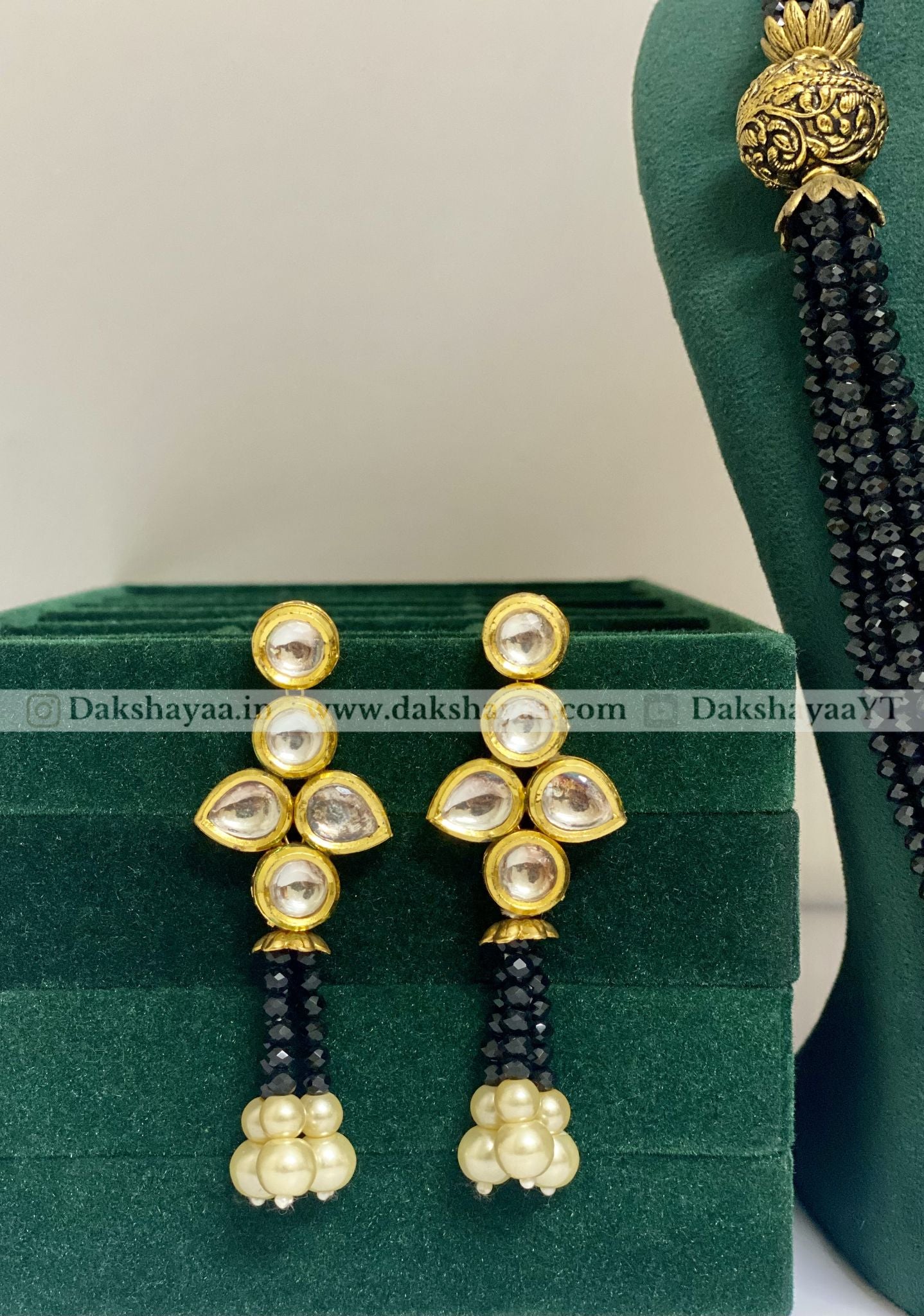 Gold and black beaded earrings on a green stand with a white background