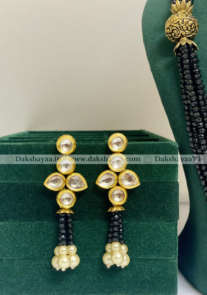 Gold and black beaded earrings on a green stand with a white background
