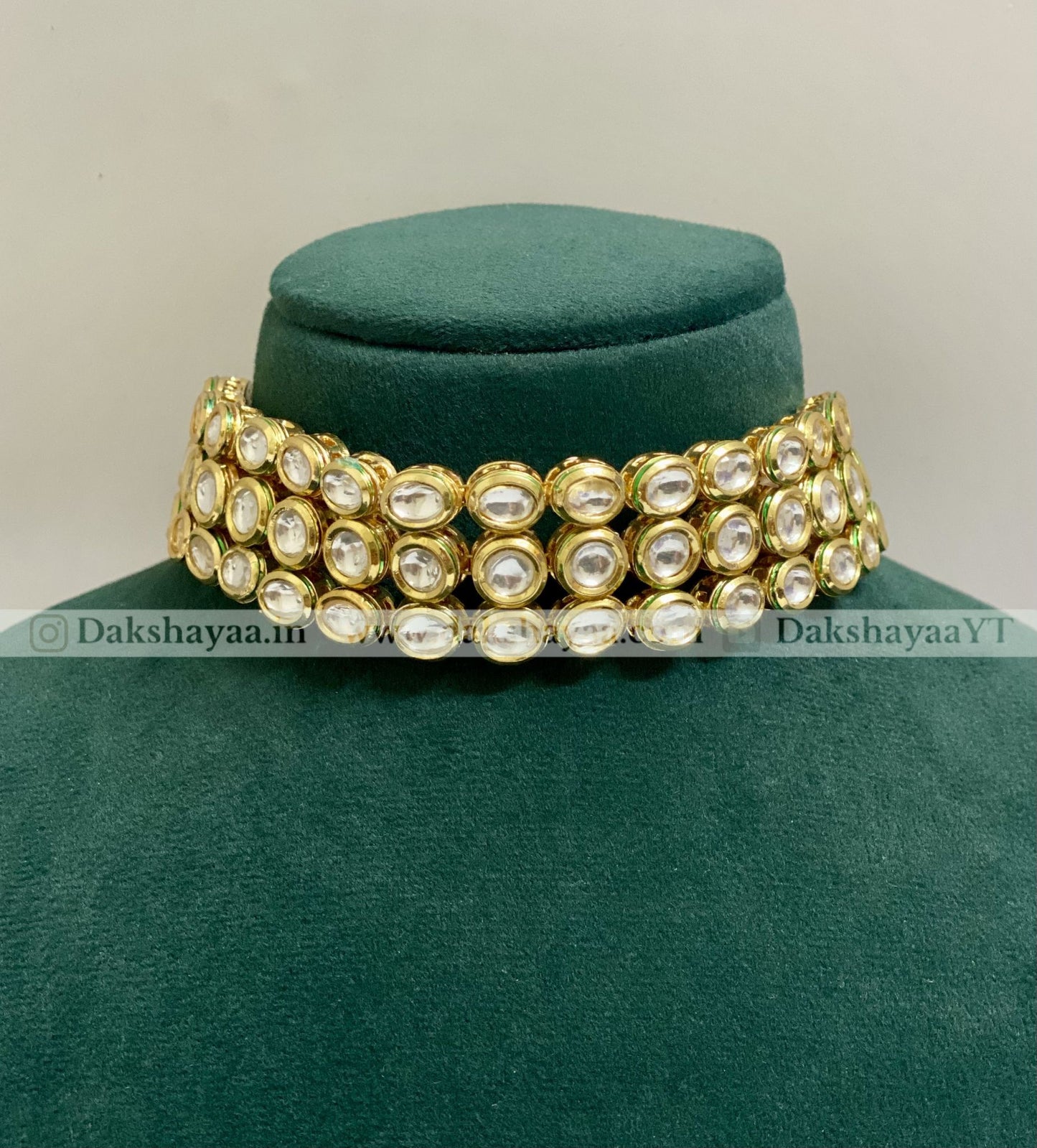 Gold and pearl choker necklace on a green velvet stand with 'Dakshayaa.in' branding.