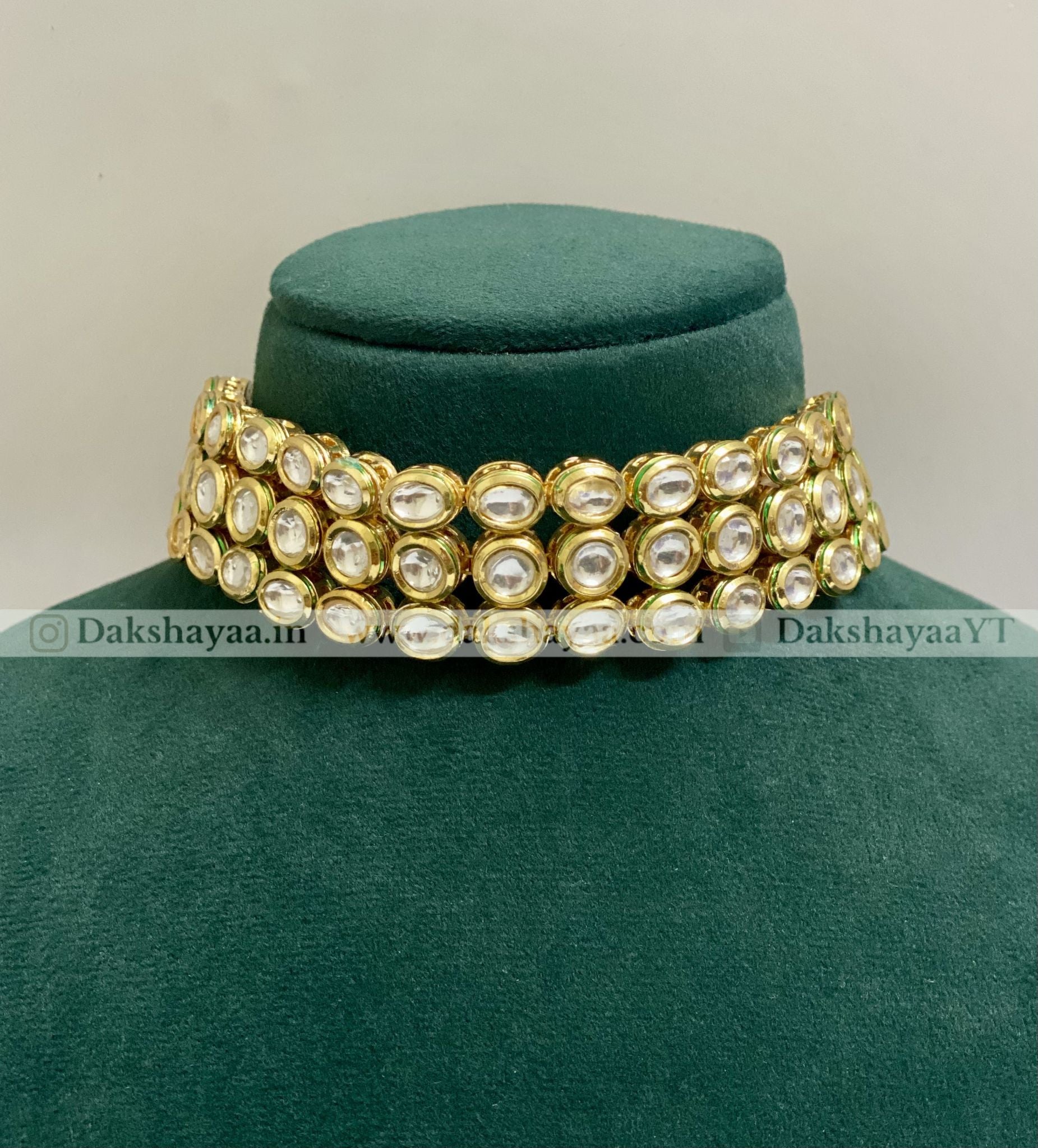 Gold and pearl choker necklace on a green velvet stand with 'Dakshayaa.in' branding.
