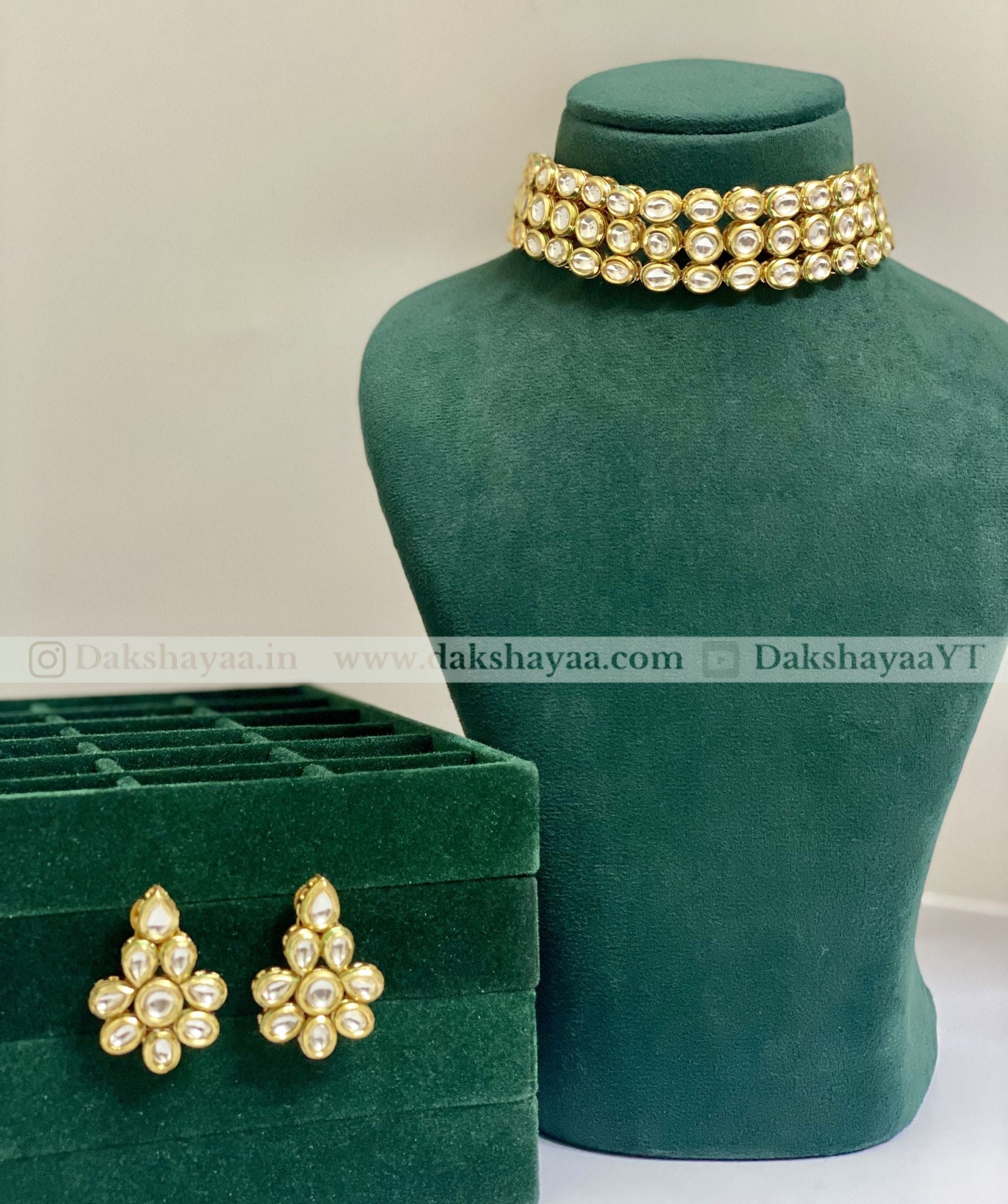 Gold jewelry set with earrings and a necklace on a green mannequin and box.
