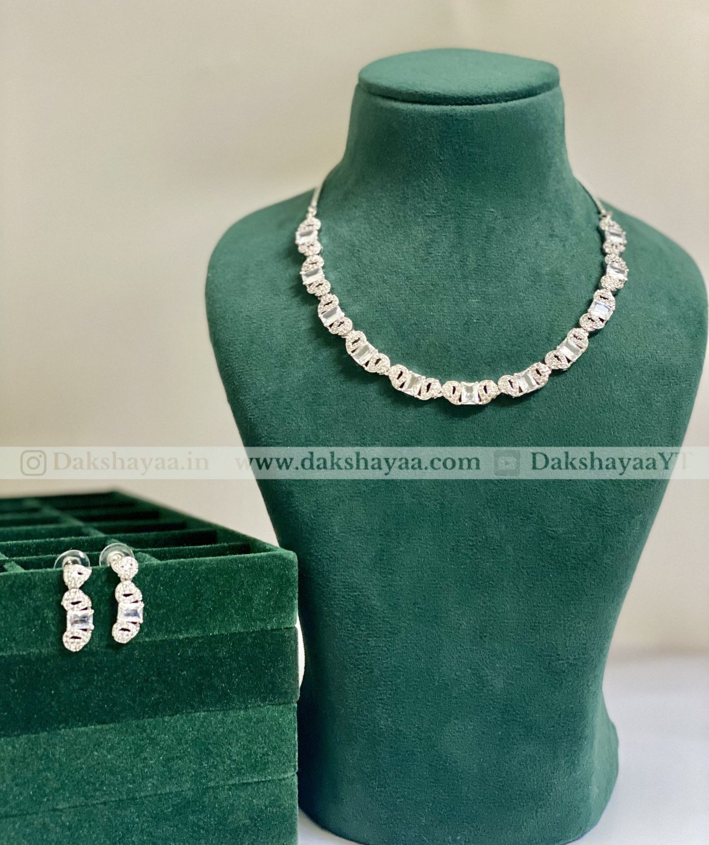 Silver necklace and earrings on a green mannequin bust with a green box in the foreground.
