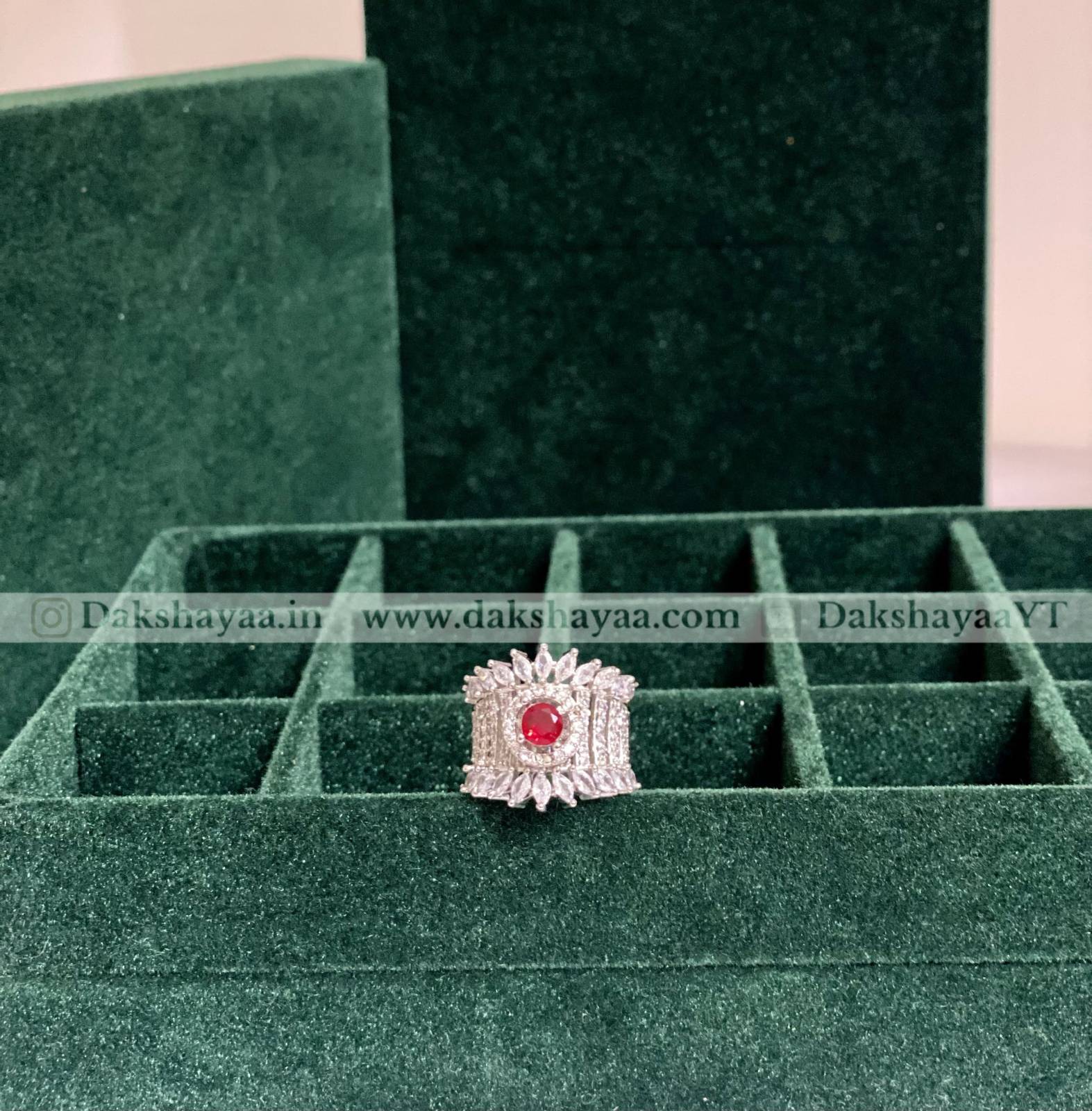 Silver ring with a red gemstone on a green velvet display box