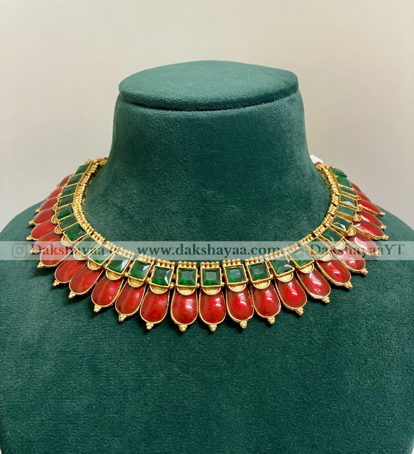 Decorative necklace with red and green stones on a green velvet stand