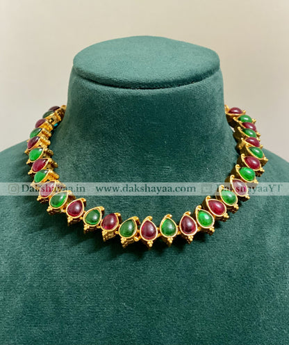 Gold necklace with green and red stones on a green velvet stand