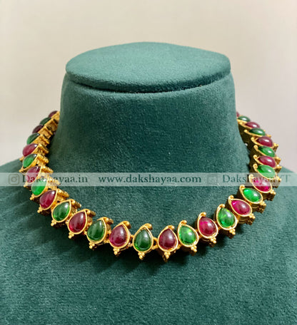 Jewelry necklace with green and red stones on a green velvet stand