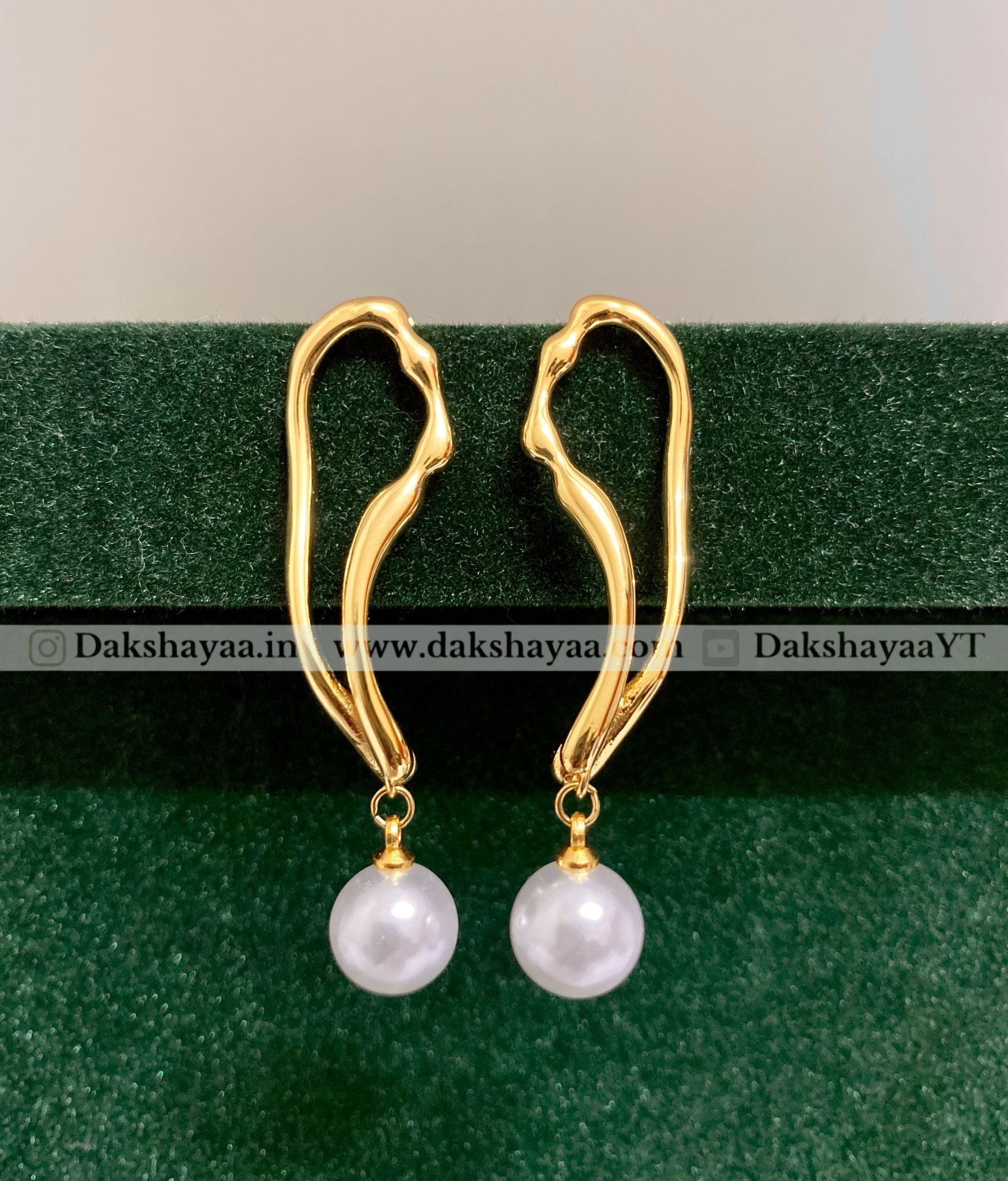 Gold earrings with pearl drops on a green background