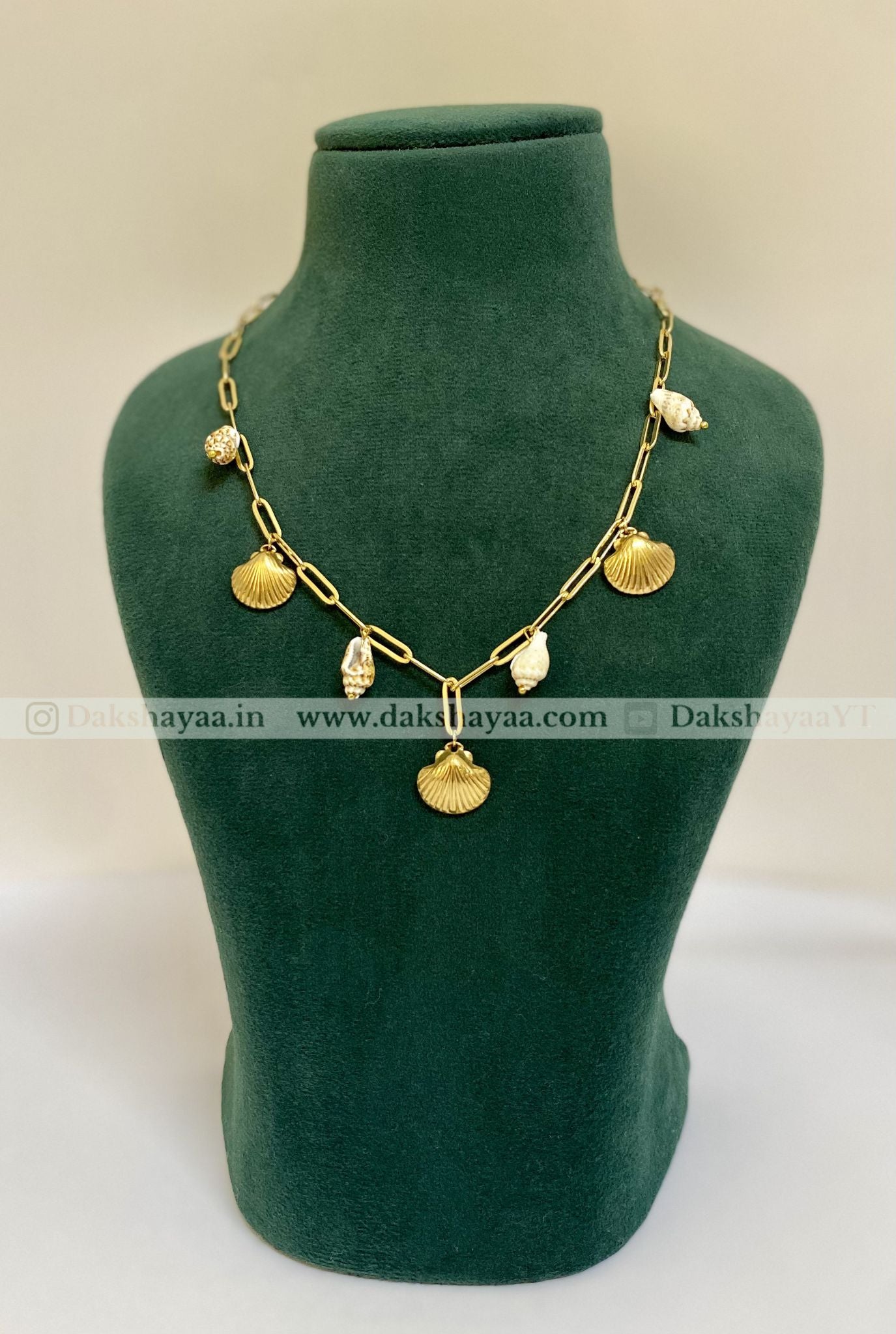 Gold necklace on a green mannequin bust with dakshayaa visible brand watermark.