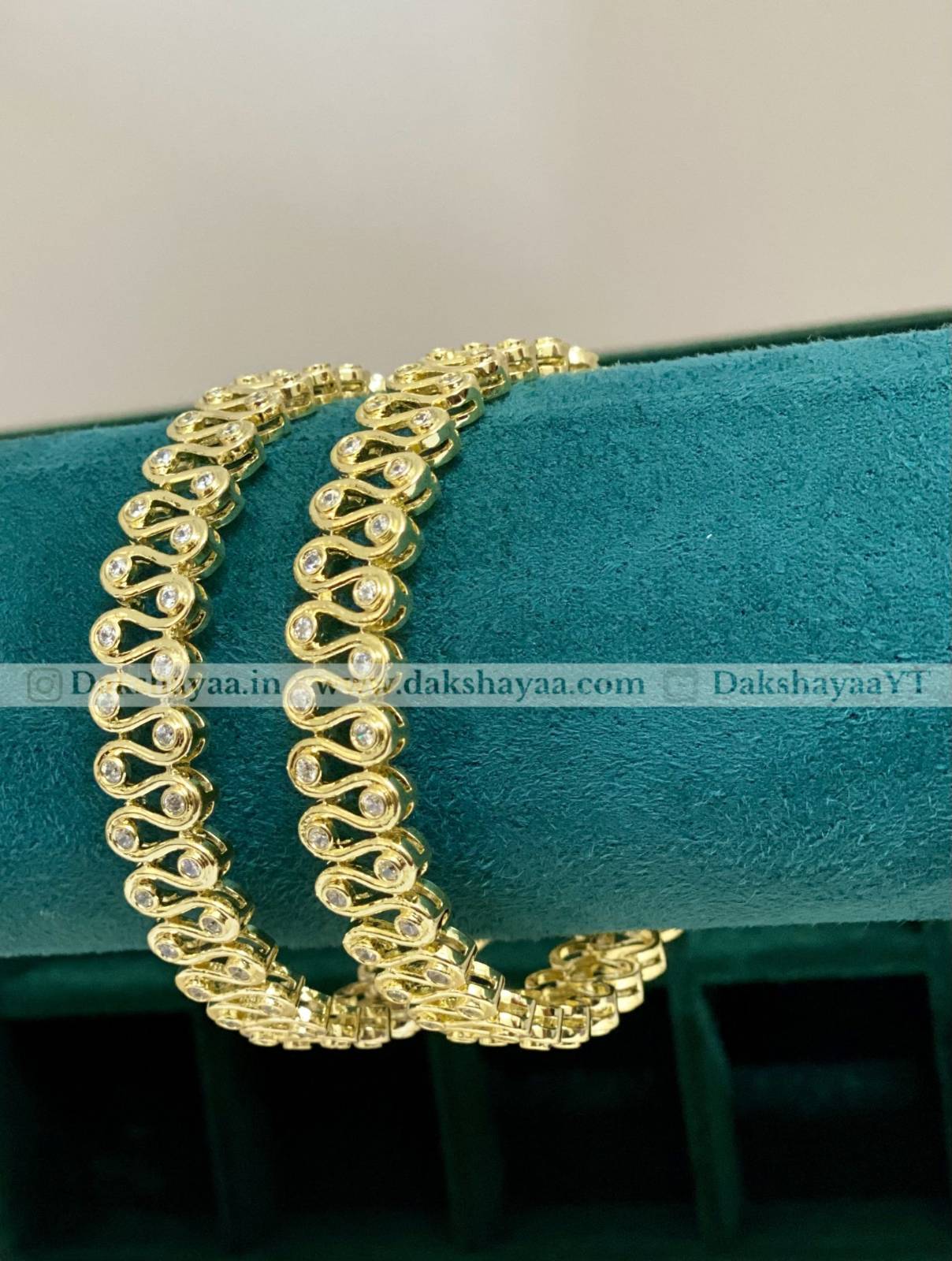 Gold bracelet on a teal cushion with 'Dakshayaa' branding.