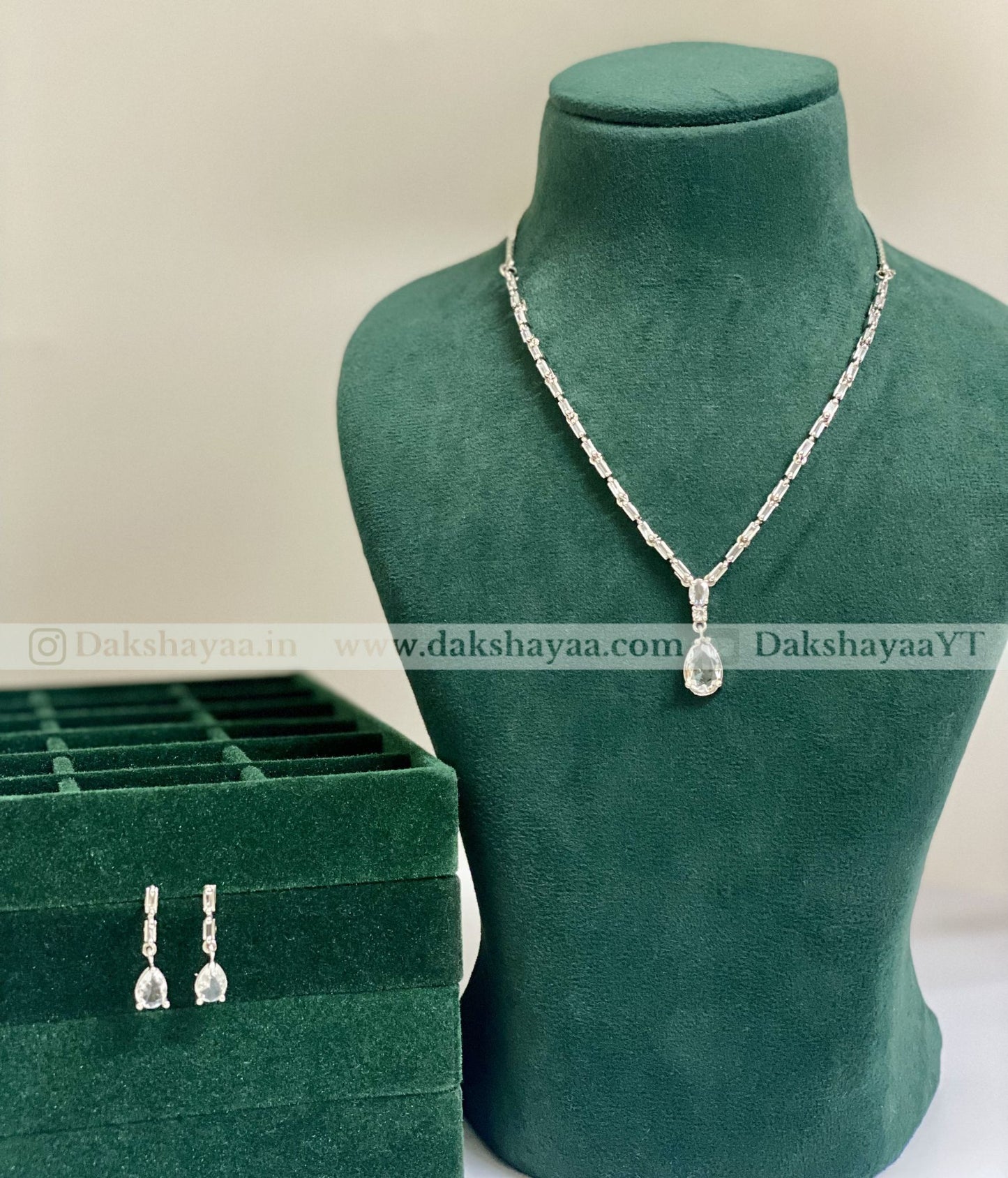 Necklace with pendant on a green mannequin bust and matching earrings in a box, with 'Dakshayaa' branding.