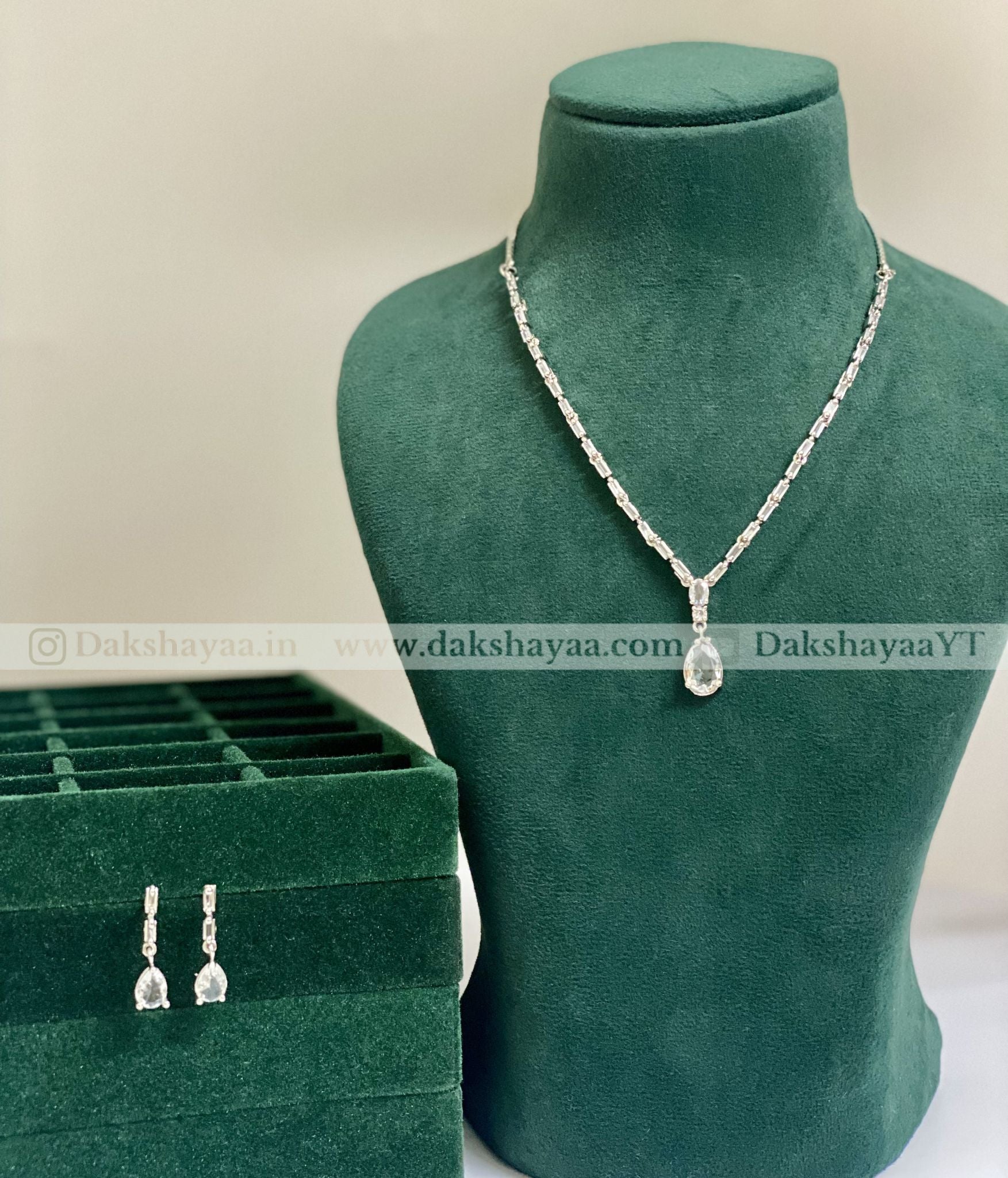Necklace with pendant on a green mannequin bust and matching earrings in a box, with 'Dakshayaa' branding.