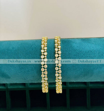 Gold hoop bangles on a teal cushion with visible branding.