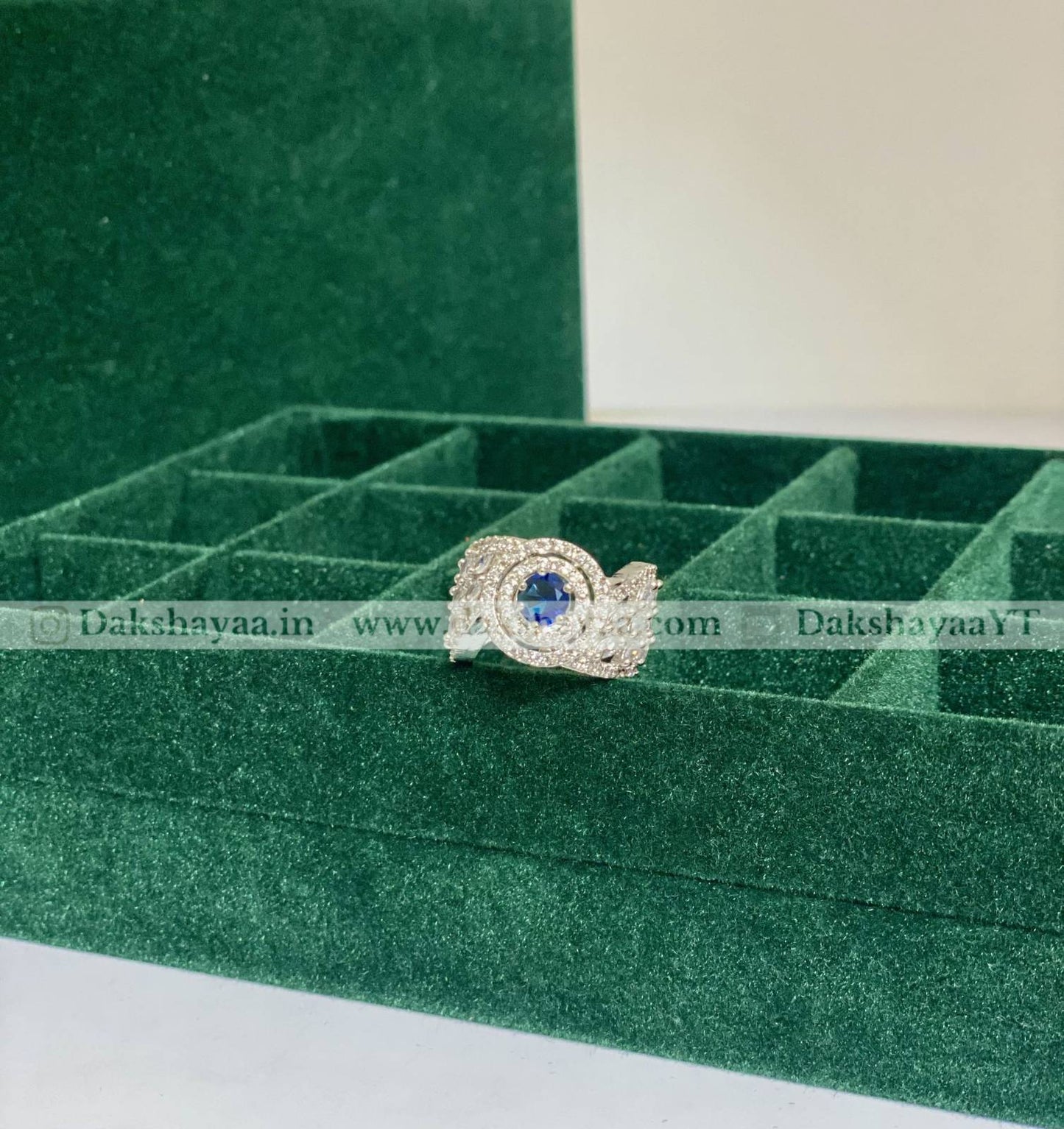 Silver ring with a blue gemstone on a green velvet display box.
