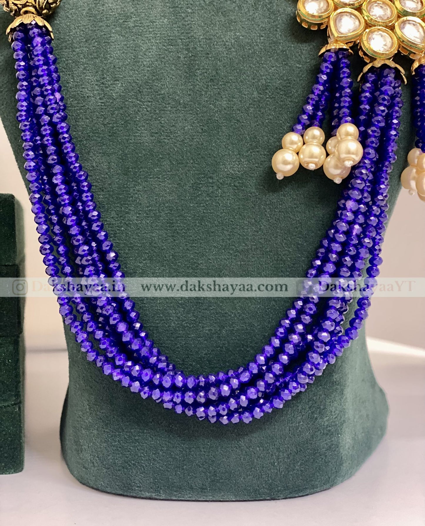 Purple beaded necklace with gold and pearl accessories on a green mannequin.