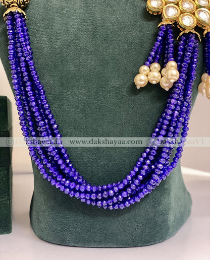 Purple beaded necklace with gold and pearl accessories on a green mannequin.