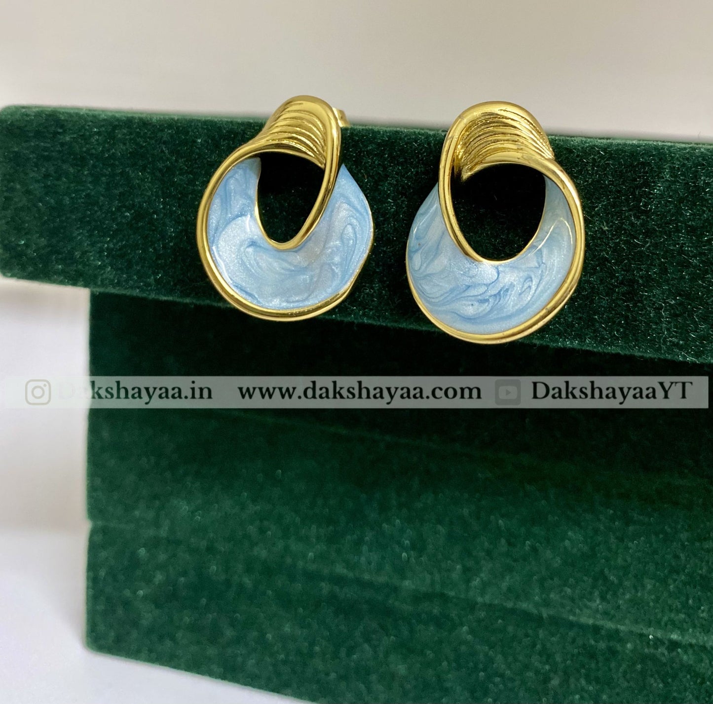 Pair of gold and blue marbled earrings on a green velvet stand.
