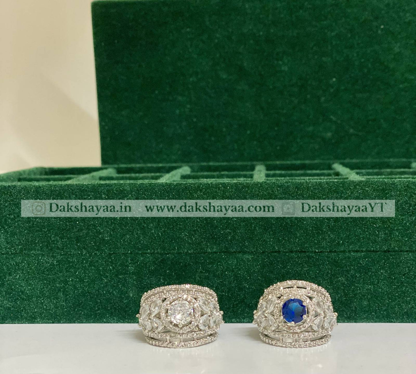 Two silver rings with a blue gemstone on a green velvet stand.