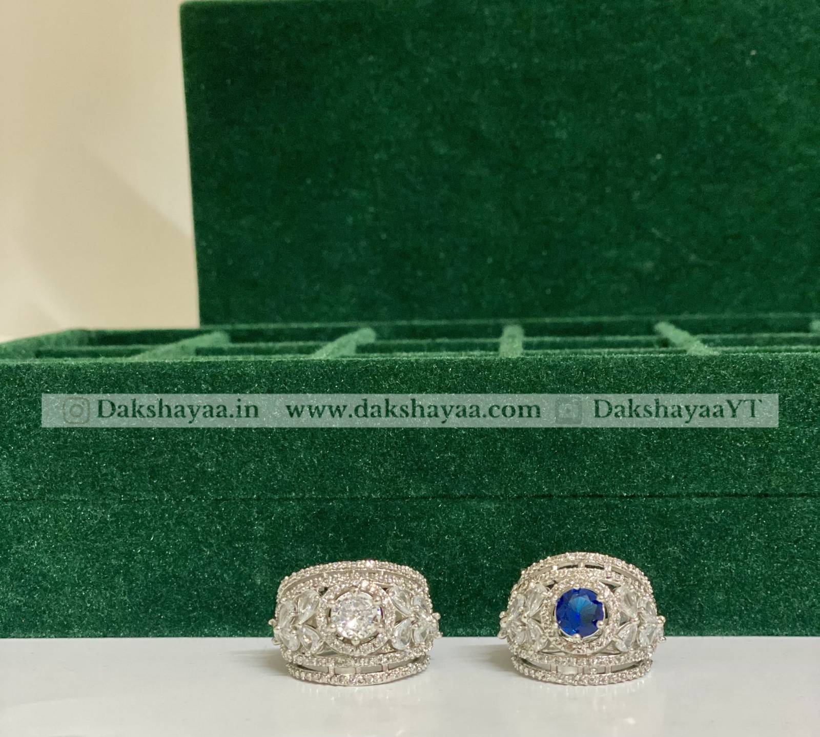 Two silver rings with a blue gemstone on a green velvet stand.