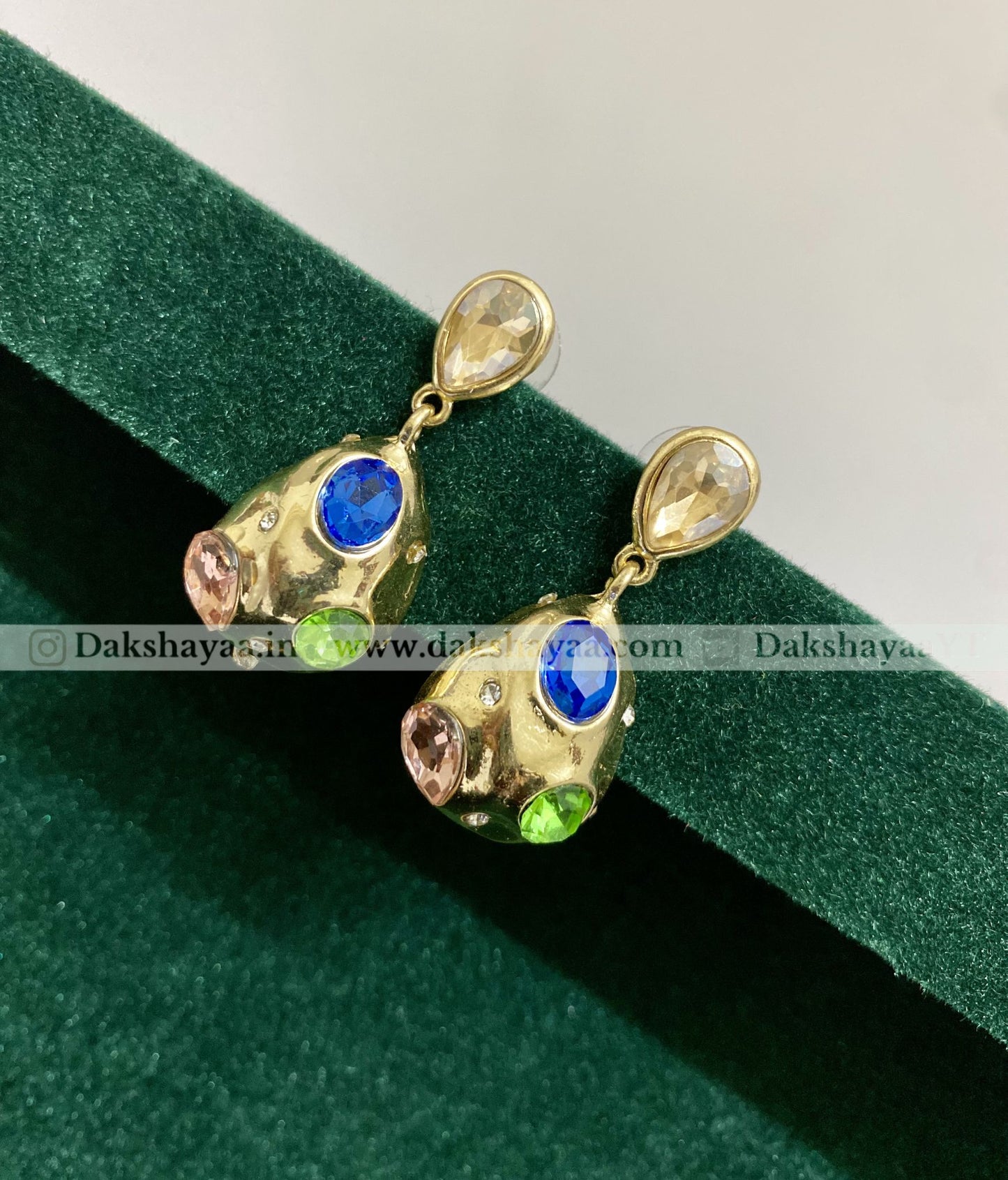 Gold earrings with gemstones on a green velvet background