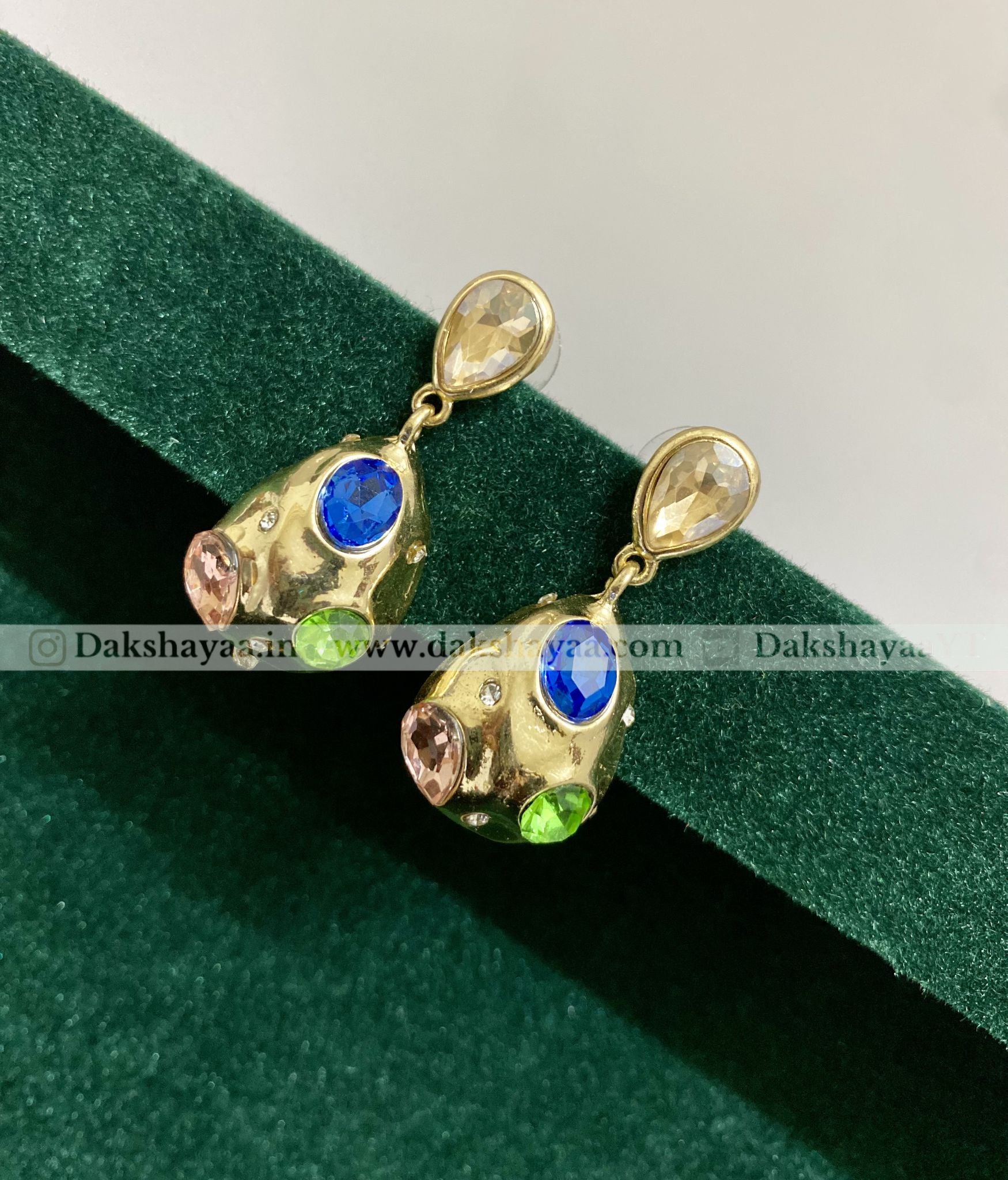 Gold earrings with gemstones on a green velvet background