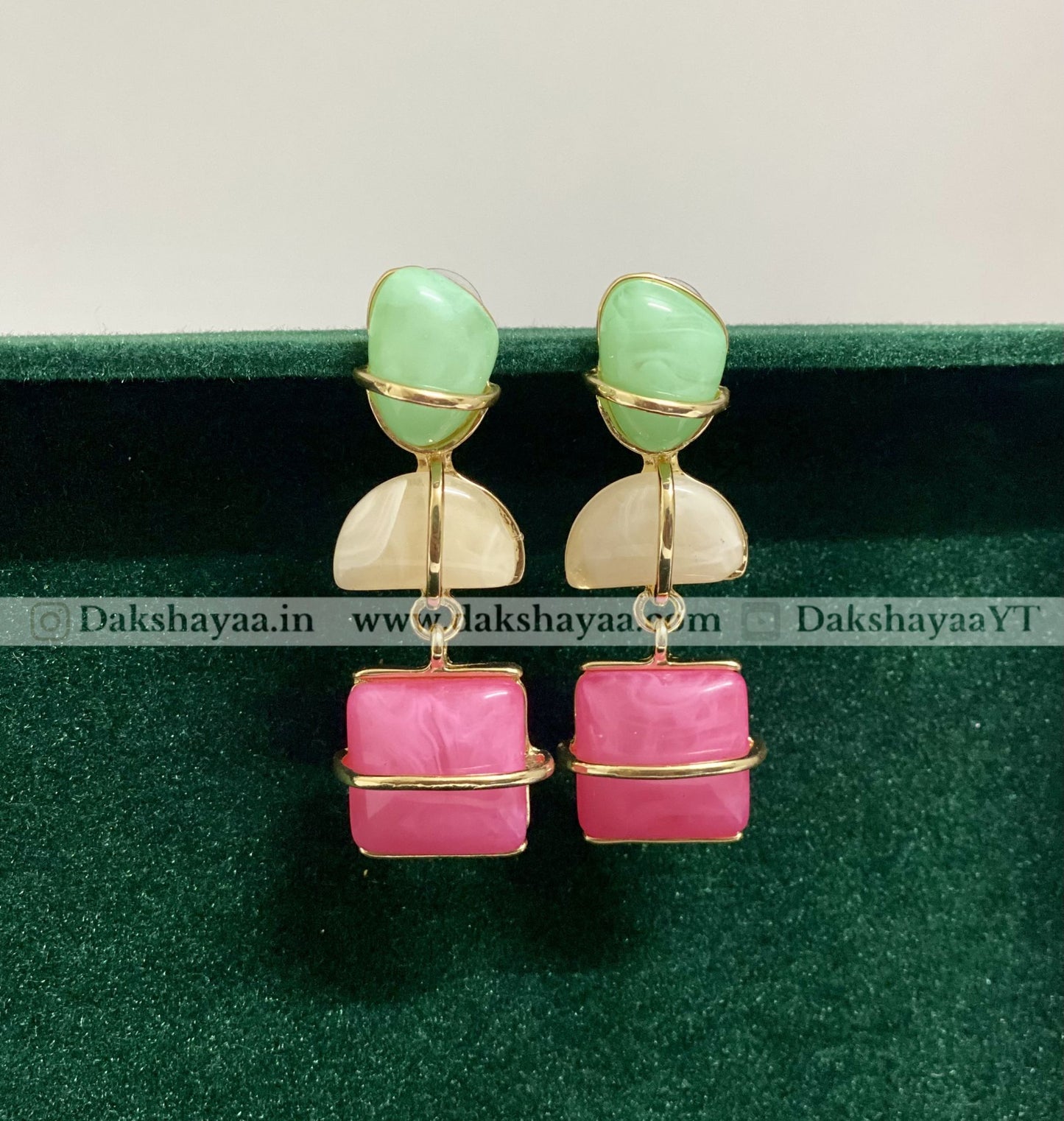 Pair of earrings with green and pink stones on a green background