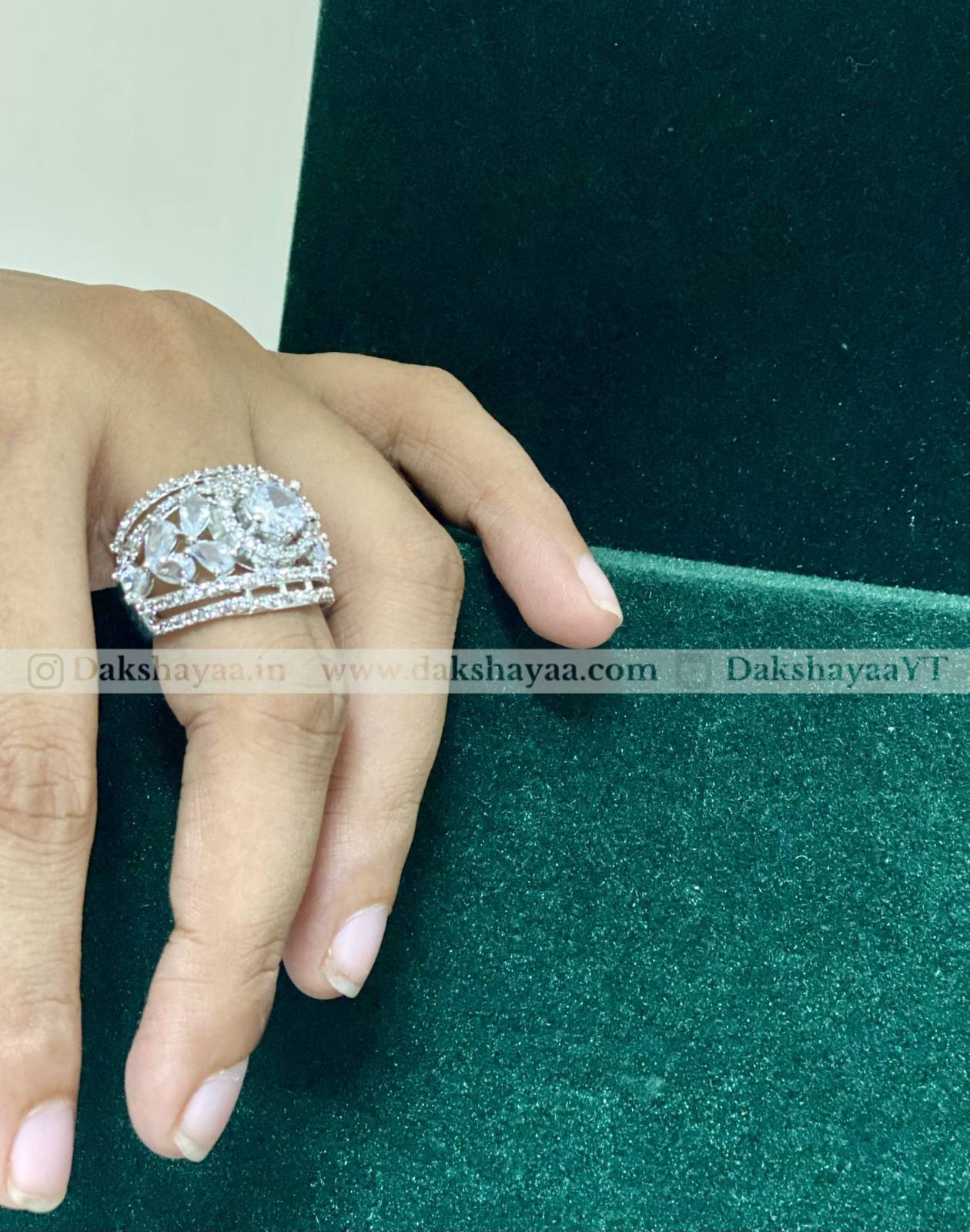Hand wearing a decorative ring on a green fabric background