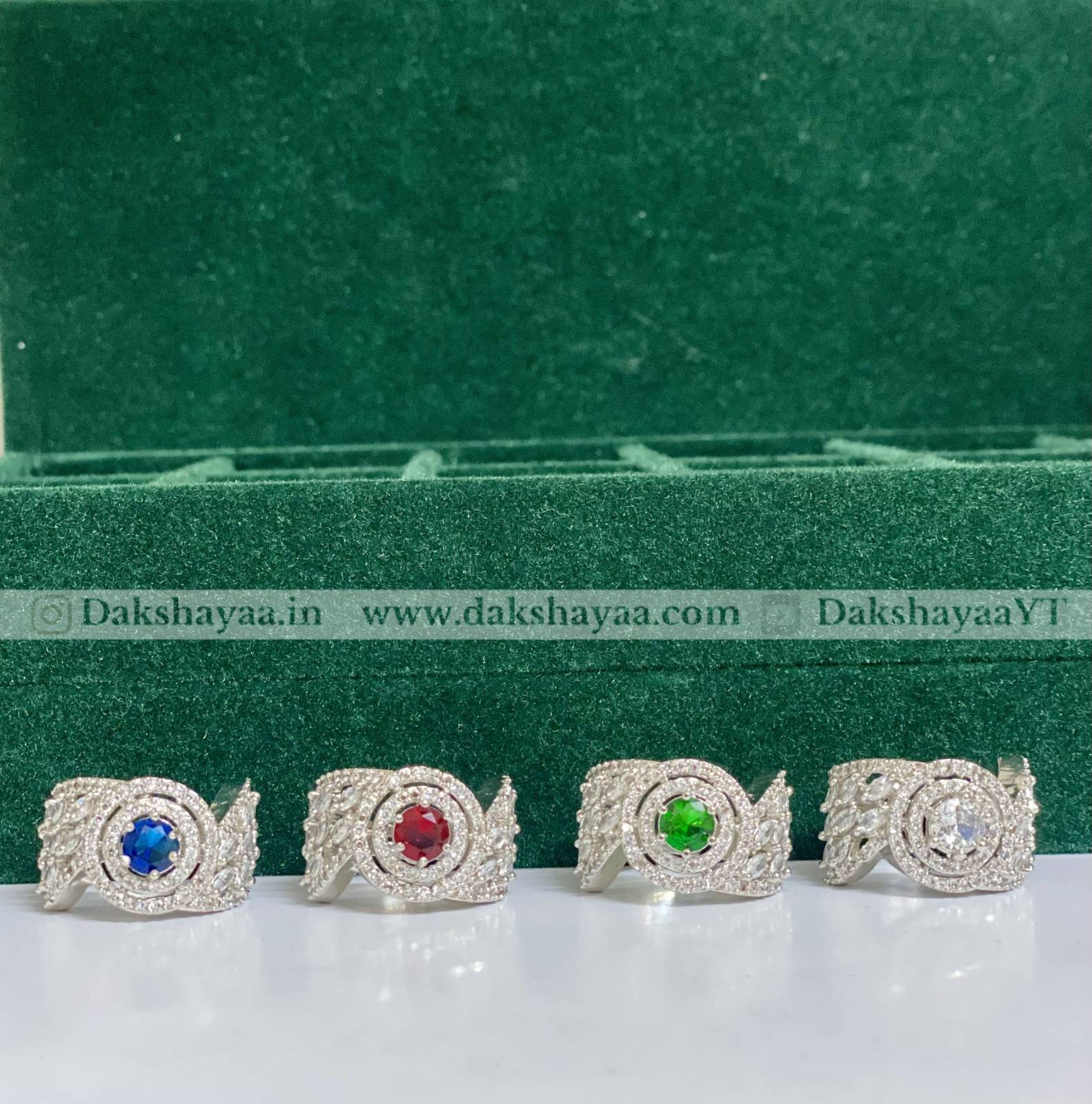 Four silver rings with colored gemstones on a green and white background