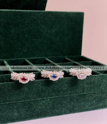 Three silver earrings with gemstones on a green velvet display box.