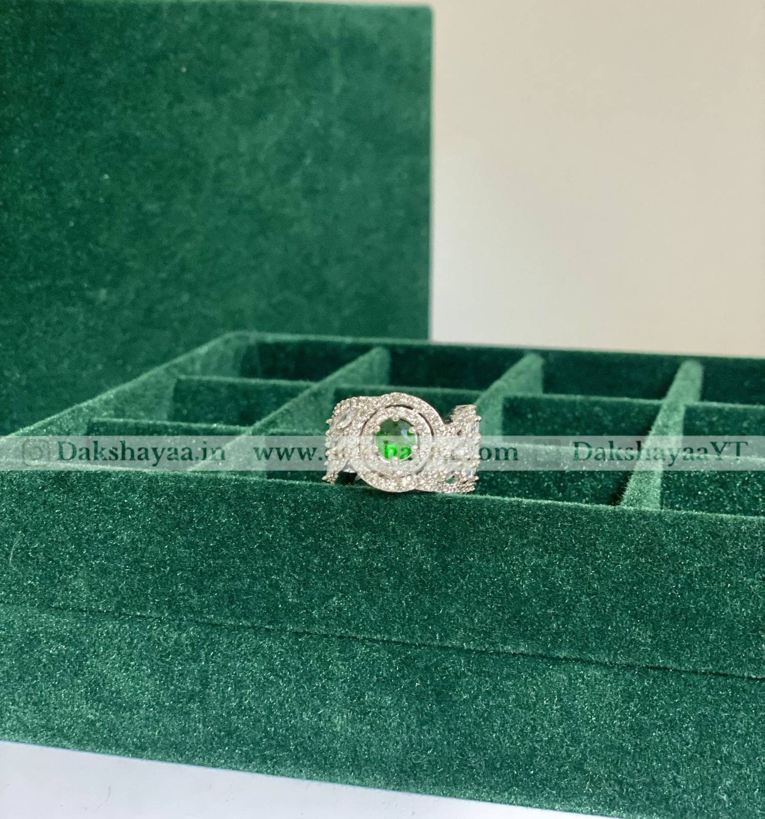 Silver ring with a green gemstone on a green velvet box