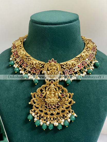 Ornate gold necklace with green beads on a green mannequin bust