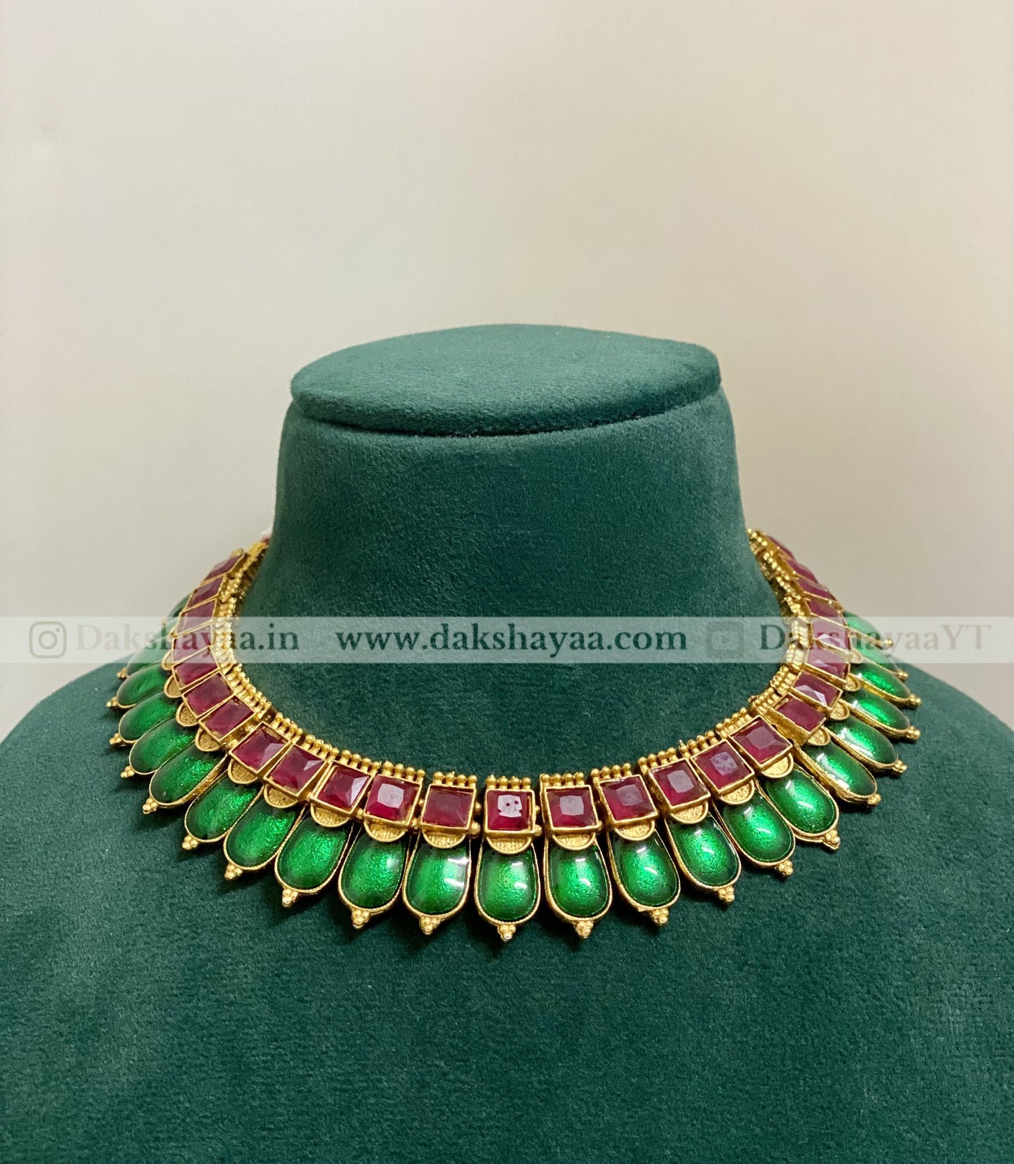 Green gemstone necklace with gold and red accents on a green velvet stand.