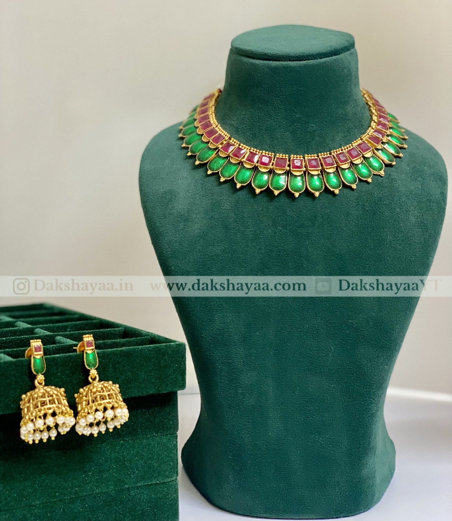 Jewelry set with necklace and earrings on a green mannequin and box, brand 'Dakshayaa' visible.