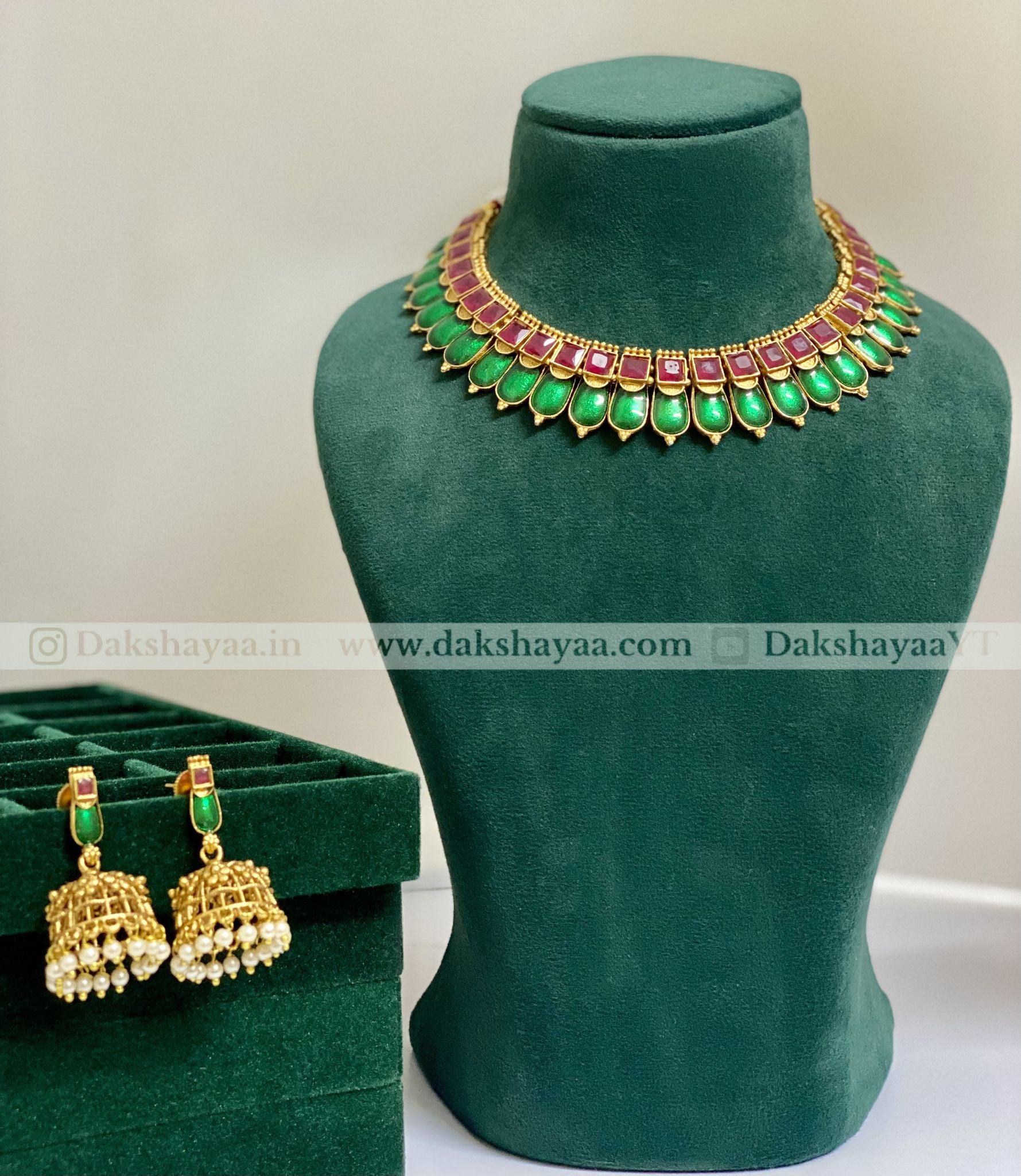 Jewelry set with necklace and earrings on a green mannequin and box, brand 'Dakshayaa' visible.