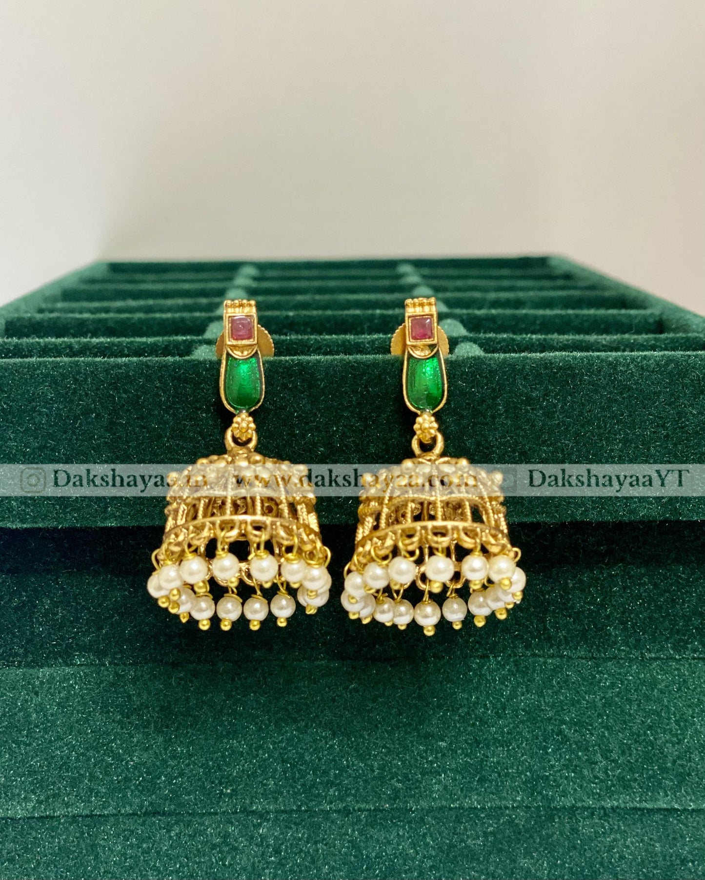Gold earrings with green and red stones on a green velvet stand