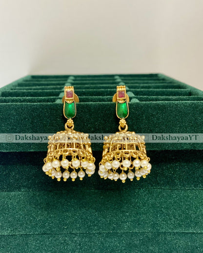Gold earrings with green and red stones on a green velvet stand