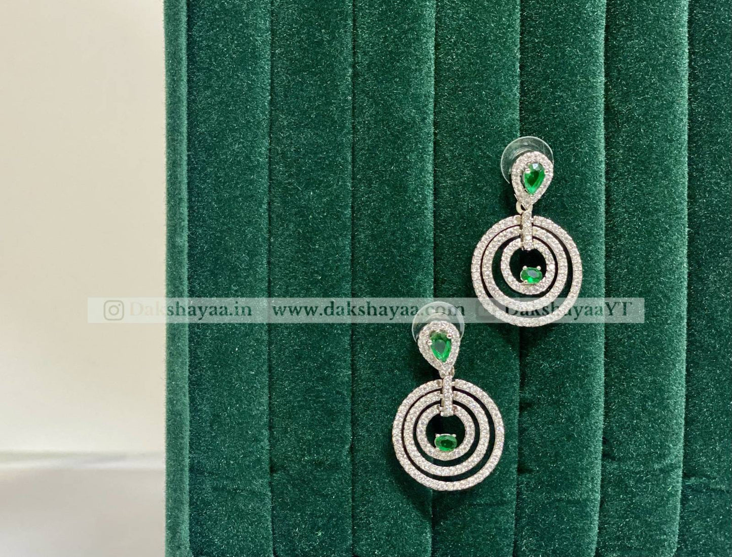 Pair of silver earrings with green gemstones on a green velvet background