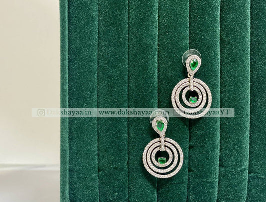 Pair of silver earrings with green gemstones on a green velvet background