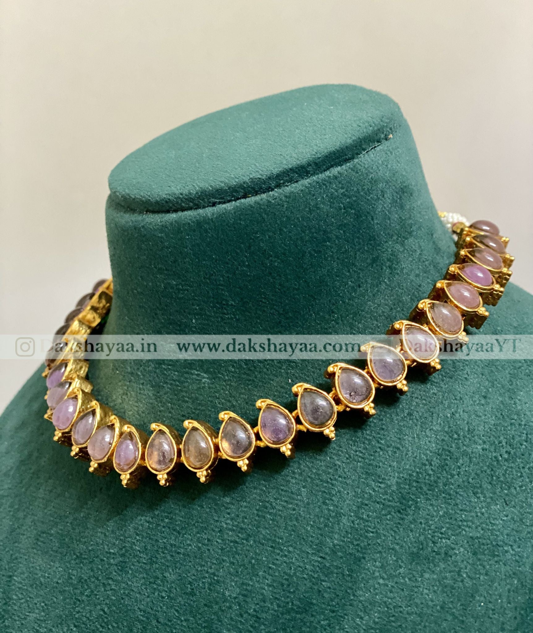Gold necklace with gemstones on a green velvet stand