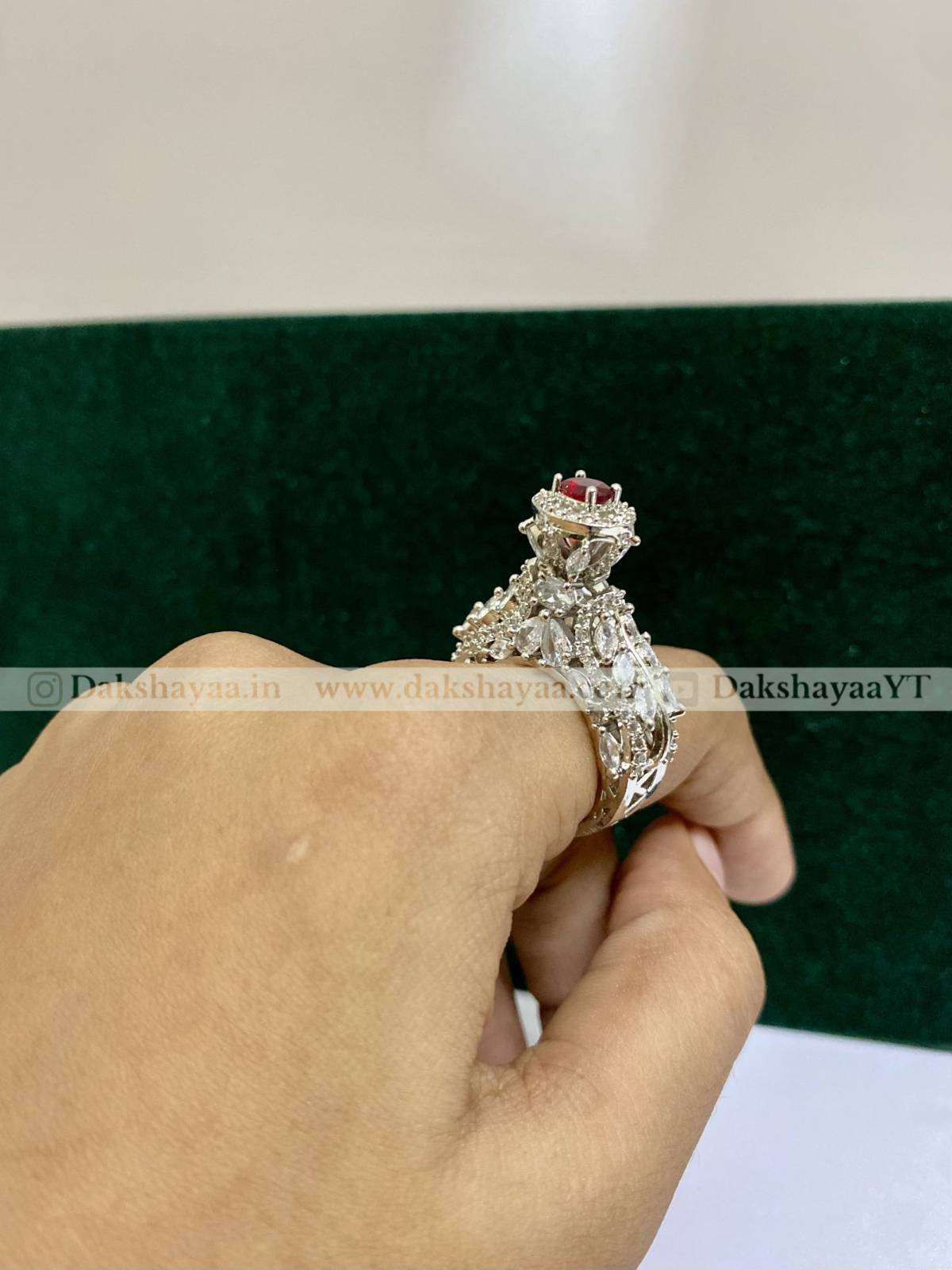 Silver ring with red gemstone held by a hand against a green fabric background