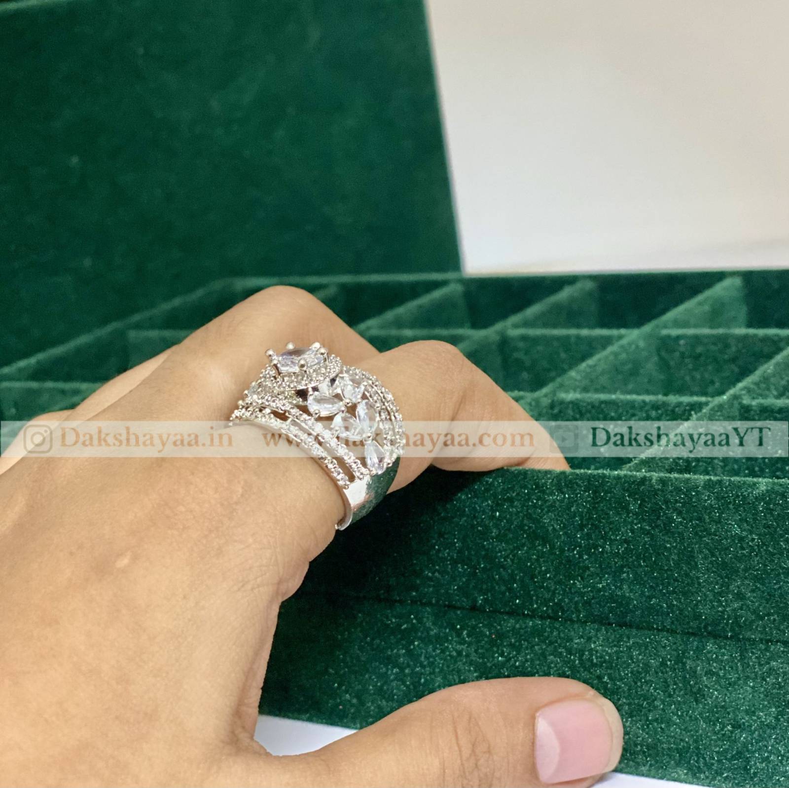 Silver ring with a large diamond on a hand against a green velvet background