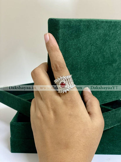 Hand wearing a silver ring with a red gemstone against a green box background