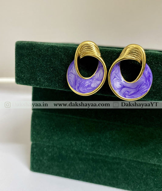 Gold and purple earrings on a green velvet stand with visible branding.