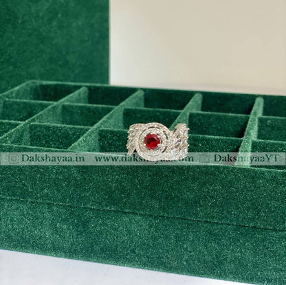Silver ring with a red gemstone on a green jewelry display box.