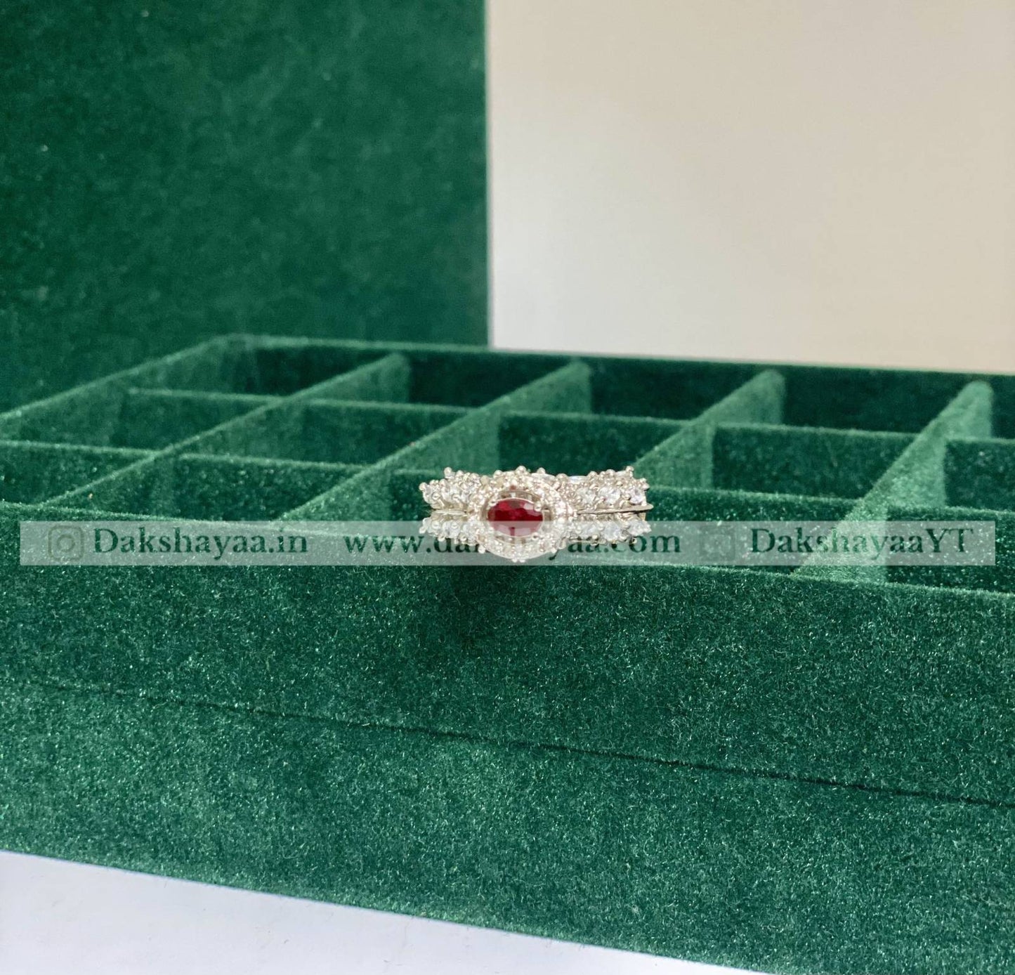 Jewelry box with a ring featuring a red gemstone on a green background