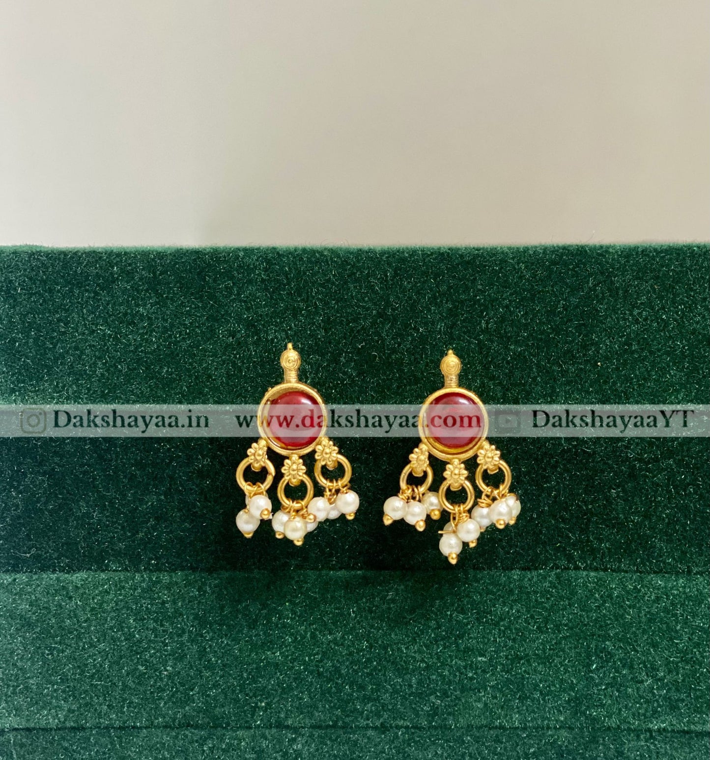 Gold earrings with red gemstones on a green velvet background