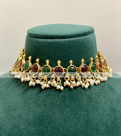 Decorative necklace with gold, red, green, and pearl elements on a green velvet stand.